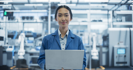Fototapeta premium Portrait of a Beautiful Electronics Manufacture Engineer Smiling, Looking at Camera. Young Asian Female Using Laptop Computer for Online Research, Monitoring Industrial Artificial Intelligence Systems