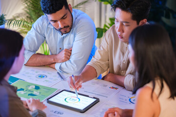 Naklejka premium diversity team brainstorming focused on ESG (environment,social,governance) with tablet or sdgs goals in a sustainable green office at night