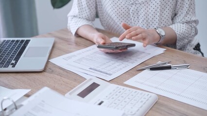 Fototapeta premium Close-up of an adult's hands with smartphone, calculator, and documents on a desk in office. Bookkeeping, finance, audit and taxes. Business concept