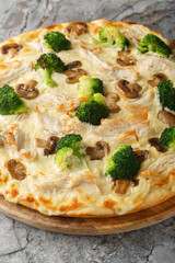 Cream pizza with chicken breast, broccoli and mushrooms close-up on wooden board on table. Vertical