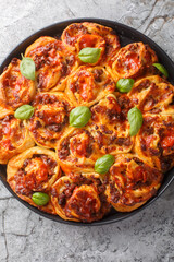 Italian pizza roll with tomatoes, cheese, sausages and basil close-up in baking dish on table. Vertical top view from above