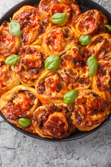Cheesy pepperoni pizza rolls with italian sausages, Mozzarella and basil closeup on the bakong dish on the table. Vertical top view from above