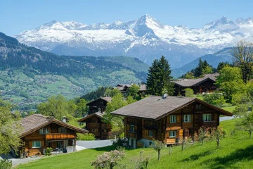 Idyllic Swiss mountain village with traditional wooden chalets against backdrop of snow-capped Alps on sunny day