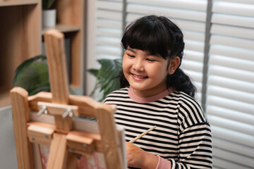 Fototapeta premium Cute Girl Painting with Acrylics on Canvas in a Bright and Cozy Home Studio, Smiling and Enjoying Creative Art Activity