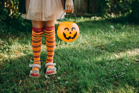 Happy Halloween day. A little cute girl in a witch costume is holding her pumpkin Jack's bucket with candy in her hand. Halloween party, kids trick or treat, close-up.