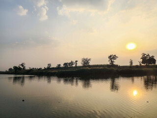 Stock photo of The beautiful sunset view at the lake, surrounded by lush green trees and vast farmland, with the trees reflection floating on waters surface, creating breathtakingly beautiful scenery