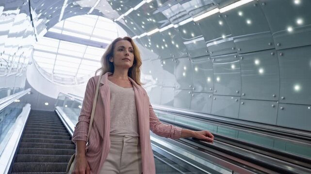 Focused Caucasian woman standing on moving escalator stairs. Going downwards. Thinking about her plans while trying not to miss next train. Looking forward while waiting to reach tube station.