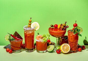 Tomato juice and vodka alcoholic cocktails with hot sauce, salt, pepper, olives and celery. Bloody mary cocktail party. Green  background, hard light
