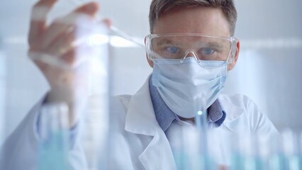 Man with safety glasses and blue mask is working with lab tubes