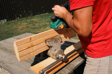 A carpenter planes a piece of wood using an electric plane. Carpenter is planing a wooden plank