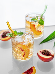 Homemade peach lemonade with ice and mint on white background. Fresh iced tea in glasses with light from the window.