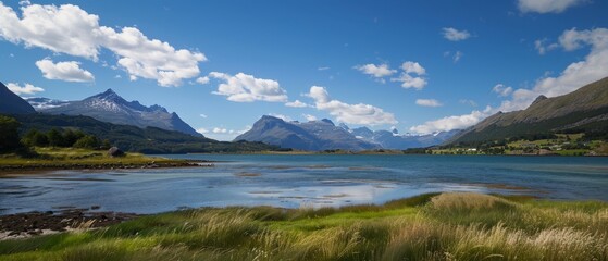 Naklejka premium A crystalline body of water nestled amongst mountains under a vast, blue sky dotted with wispy clouds Verdant grass blankets the landscape in the foreground