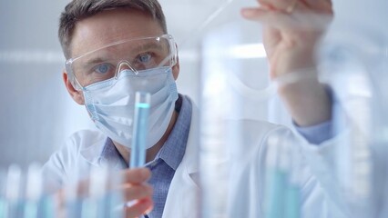 Man with safety glasses and blue mask is working with lab tubes