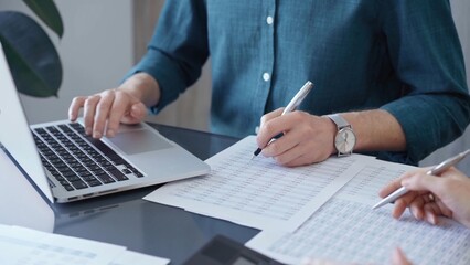 Fototapeta premium Business people professionals analyzing data on laptop. Close-up of auditor's hands reviewing financial spreadsheets in a modern office setting. Finance teamwork