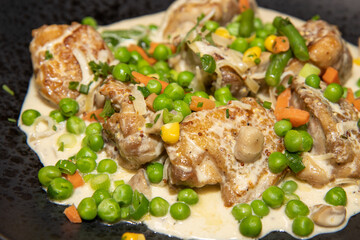 A close up photo of a delicious plate of Creamy Chicken with Spring Vegetables on a black plate