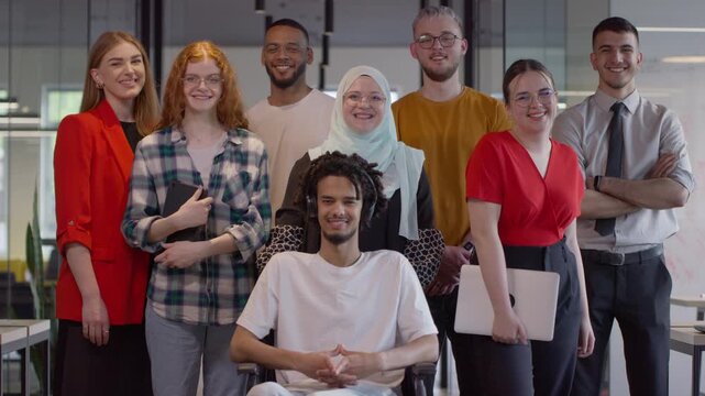 A diverse group of young business people congregates within a modern startup's glass-enclosed office, featuring inclusivity with a person in a wheelchair, an African American young man , and a hijab