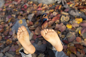 bare feet of child close-up against background of multi-colored fallen dry leaves and shoes. carefree childhood, freedom, walks, enjoying the warm autumn. warm-up and rest for the legs. Indian summer