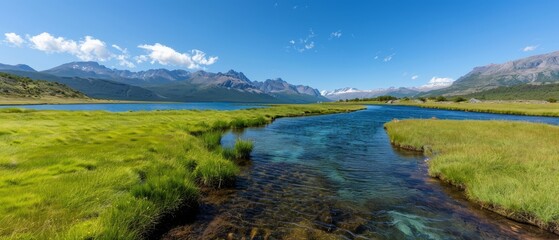  A stream runs through a lush green field, bordering another, backed by mountain ranges