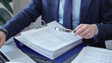 Adult businessman or auditor examining documents with magnifying glass. Professional in a suit...