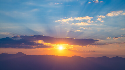 The setting sun over the mountains, the beautiful sun's rays shine through the clouds, the natural background, freedom, tranquility and peace