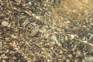 multi-colored stones under water on the sea, river. Natural background of stones, glare on the water