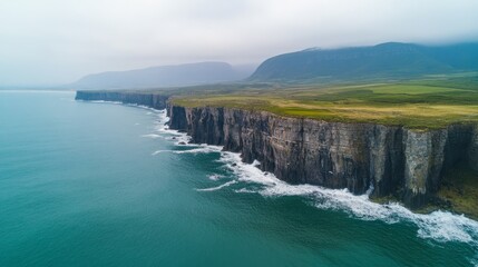 Obraz premium Aerial view of dramatic cliffs along a rugged coastline with crashing waves.