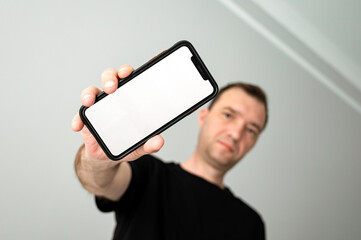 A man is holding a smartphone against a monochromatic backdrop. The screen is blank, ready to receive content. Copy space