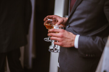 man in a tuxedo is holding two glasses of alcohol, a groom or a businessman