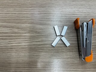 An orange stapler and a few metal staples placed on a wooden desk, ready for office use.