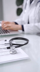 Stethoscope is lying on the glass table while doctor woman is working with laptop computer on the...