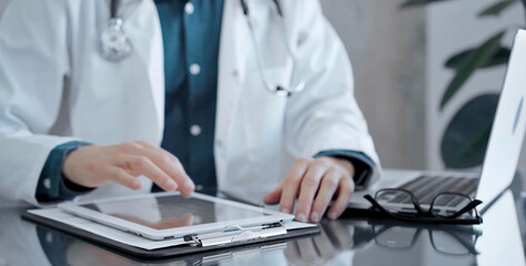 Doctor man wearing white medical coat over a green shirt is using tablet computer making some notes, close up of hands. Medicine and health care