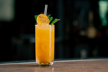 on dark background a tall glass glass with a yellow-orange cocktail decorated with mint and dried...