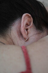 Close-up of a woman's ear with an earring from the back lying on the beach in a red dress