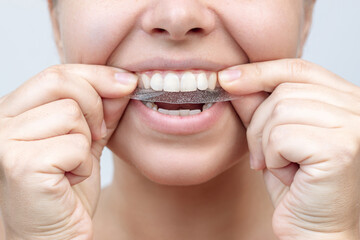 Cropped shot of a young caucasian smiling woman holding a 3d transparent teeth whitening strip to...