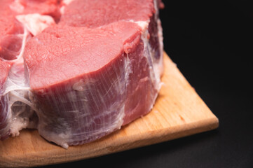 Raw large piece of pork meat served on wooden cutting board, close-up. Main ingredient in cooking