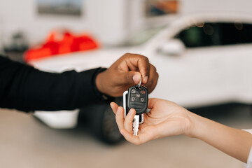 Cropped shot of unrecognizable female buyer getting car key and congratulation from black auto dealer male while buying new auto in dealership. Woman car owner during handing over keys at showroom.