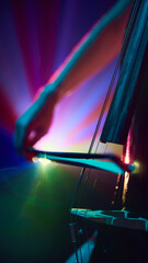 Close up photo of bow slightly, slides over double bass strings in dramatic stage smoke and vibrant...