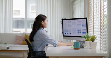 Smart Gen Z tech talent workforce typing SEO sale report on desktop PC happy work easy relax at home office. Remote WFH reskill upskill job MBA study of young people asia woman examine big data graph.