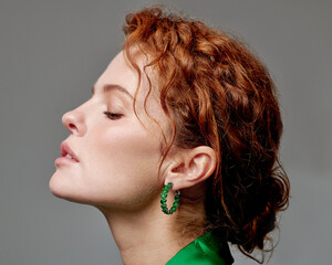 The beautiful red-haired model, dressed in an elegant outfit with jewelry, smiles and radiates joy.