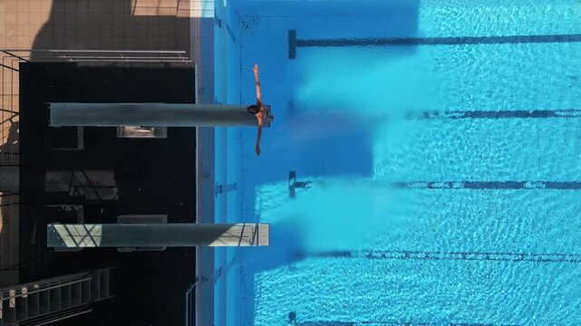 Drone footage capturing a diver mid-air performing a tuck dive above a clear blue pool, with stunning reflections and precise timing. Perfect for sports, aerial, and aquatic-themed projects