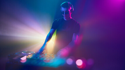 Obraz premium DJ in headphones immersed in of vibrant lights, mixing beats as colors pulse around him, creating an electrifying atmosphere. Concept of modern music and technology, party, disco, nightlife.