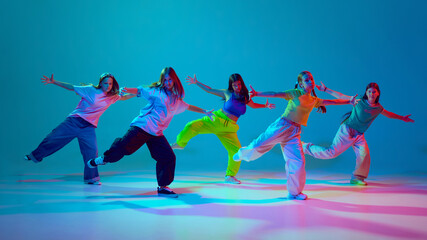 Self-expression through dynamic dance. Young girls, teens performing hip hop on stage against cyan...