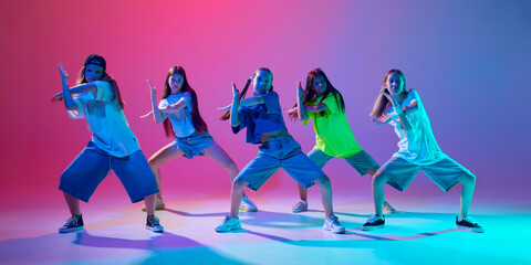 Group of children energetically showcase their hip hop moves, girls making dynamic performance against gradient pink purple background in neon light. Concept of modern dance styles, youth culture