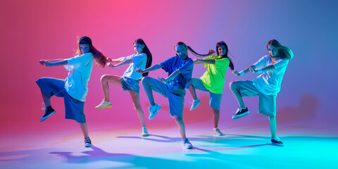 Girls in oversized streetwear dancing hip hop, making energetic performance against gradient pink purple background in neon light. Concept of modern dance styles, youth culture, active lifestyle