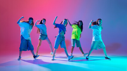 Energetic young girls, children performing dynamic hip hop dance against gradient pink purple...