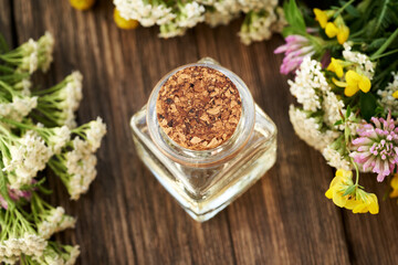 A bottle of aromatherapy essential oil with fresh yarrow and colorful summer flowers