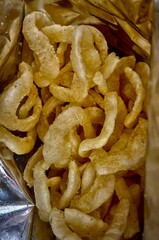 The image shows a group of light yellow, ring-shaped snacks arranged on a white surface, suggesting a crunchy texture and savory flavor.