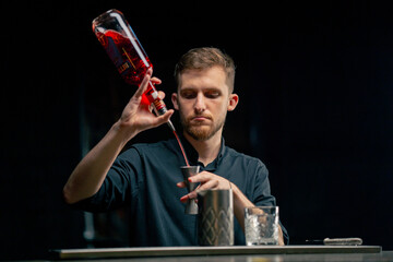 male bartender hands holding bottle and masterfully pours beverage into steel jigger on a black...
