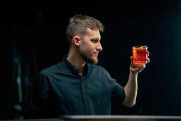 in a bar on a black background handsome young bartender in a black shirt stands over the bar...
