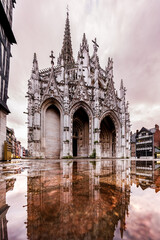 ROUEN, NORMANDY, FRANCE - 2024: Church of Saint Maclou, west facade, main entrance, cobbled Barthelemy square, pedestrian area in historical center, reflection of church in puddles